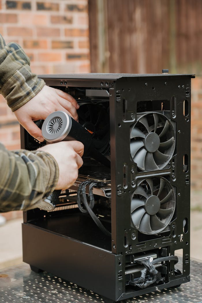 About Hands cleaning a desktop PC case with an electric duster outdoors.